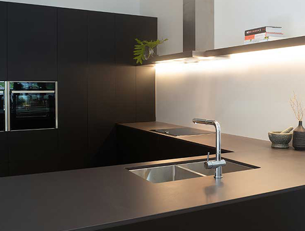 Modern kitchen with dark cabinets, stainless steel sink, sleek counters, and under-cabinet lighting.