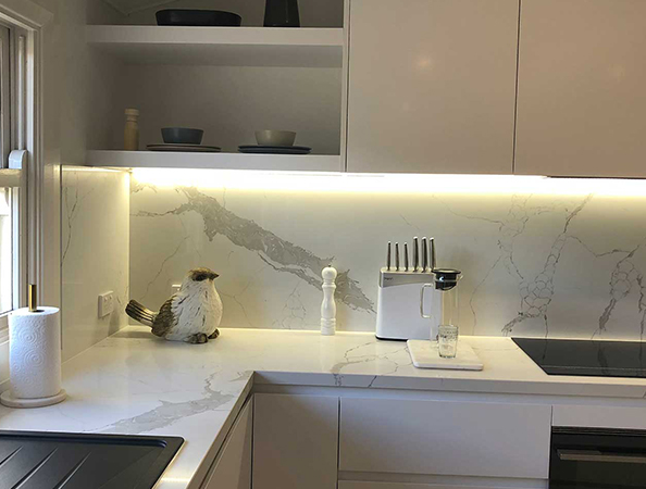 Modern kitchen with marble countertops, bird figurine, pepper grinder, coffee machine, and knife set under LED lights.