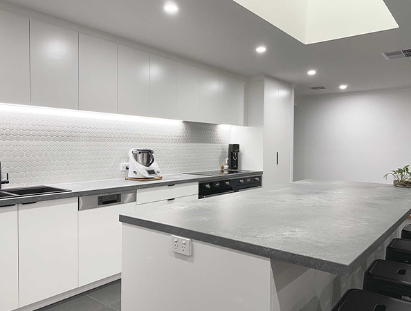 Modern kitchen with white cabinets, gray countertops, island, and under-cabinet lighting.