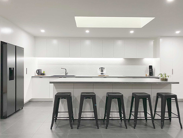 Modern kitchen with a long island, five black stools, white cabinets, and a skylight.