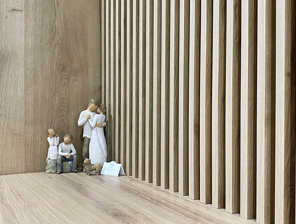 Wooden figurines of a family and dog sit in a wooden corner with vertical slats on the right side.