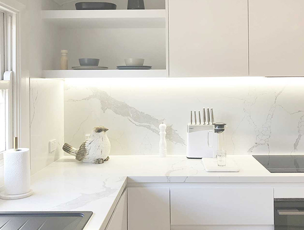 Bright white kitchen with marble counters, black stove, knife set, and decorative bird on counter near window. Bright white kitchen with marble counters, black stove, knife set, and decorative bird on counter near window.