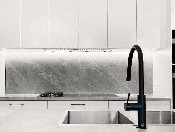 Modern kitchen with a black faucet, dual sink, gas stove, and a gray marble backsplash under white cabinets.