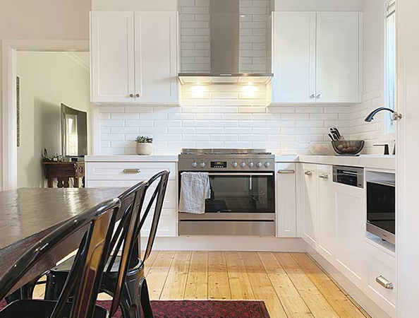 Modern kitchen with white cabinets, stainless steel appliances, and a wooden dining table with black chairs.
