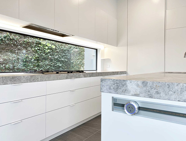 Modern kitchen with white cabinets, grey countertop, and a large window showcasing greenery.