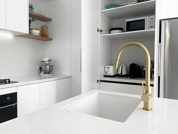 Modern kitchen with a white countertop, gold faucet, and open shelving with appliances like a mixer and toaster. Modern kitchen with a white countertop, gold faucet, and open shelving with appliances like a mixer and toaster.