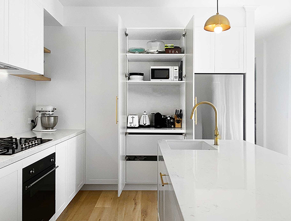 Modern white kitchen with open pantry, appliances, island with sink, brass fixtures, and wooden flooring. Modern white kitchen with open pantry, appliances, island with sink, brass fixtures, and wooden flooring.