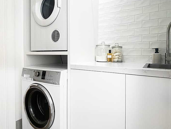 Modern laundry room with stacked washer and dryer beside a white counter and sink, jars on counter. Modern laundry room with stacked washer and dryer beside a white counter and sink, jars on counter.
