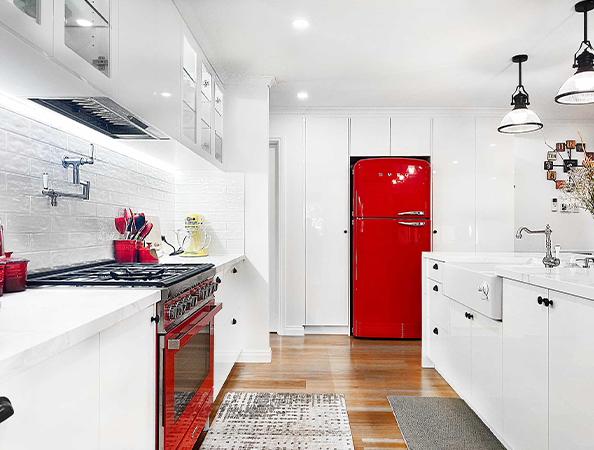 Modern kitchen with red appliances, white cabinets, wooden floor, and hanging pendant lights.
