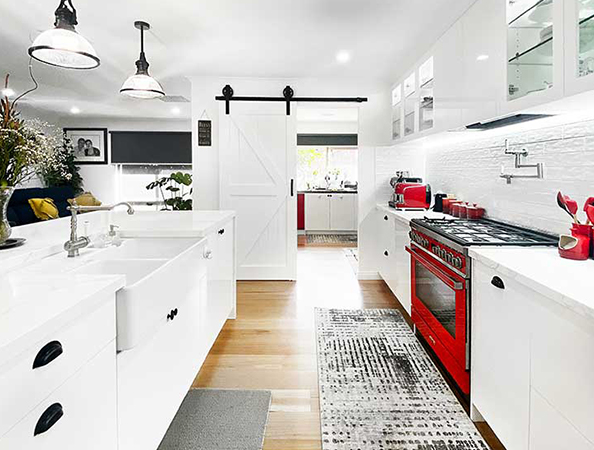 Bright kitchen with white cabinets, a red stove, farmhouse sink, pendant lights, and a sliding barn door.