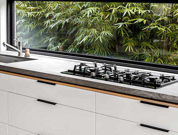 Modern kitchen with white cabinets, a gray countertop, a gas stove, and a large window view of bamboo plants.