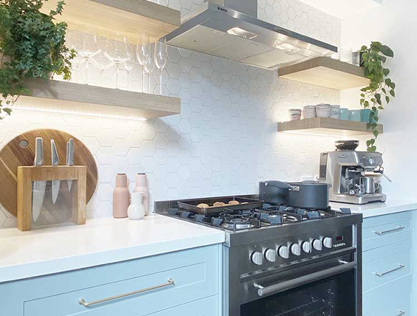 Modern kitchen with a stove, hexagonal tile backsplash, floating shelves, and potted plants.