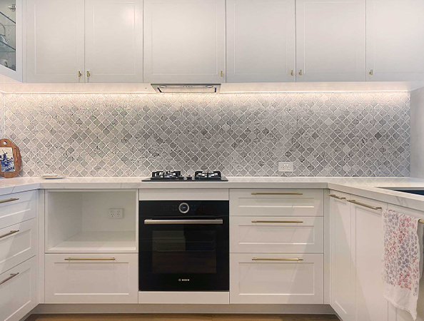 Modern white kitchen with marble backsplash, gas stove, oven, and under-cabinet lighting. Towel on the right.
