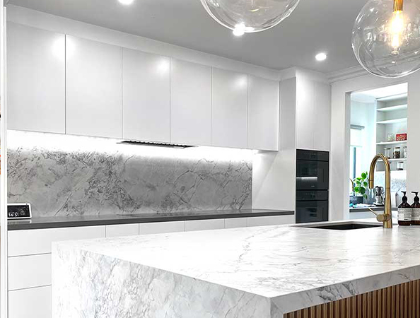 Modern kitchen with white cabinets, marble countertops, and pendant lights.