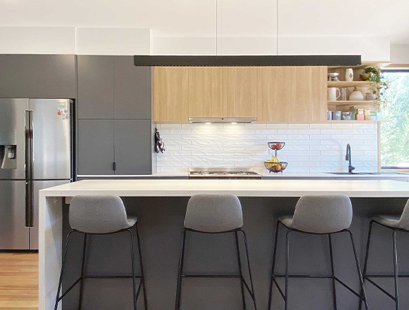 Modern kitchen with gray cabinets, a white counter, bar stools, and natural light from a large window.
