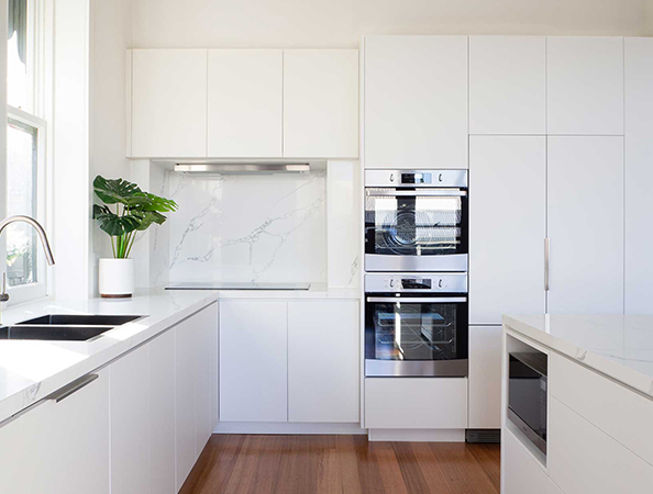 Modern white kitchen with built-in ovens, a potted plant, and wooden flooring. Bright and minimalist design. Modern white kitchen with built-in ovens, a potted plant, and wooden flooring. Bright and minimalist design.