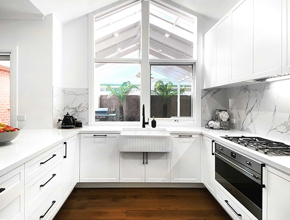 Modern white kitchen with large window, marble backsplash, farmhouse sink, and stainless steel appliances. Modern white kitchen with large window, marble backsplash, farmhouse sink, and stainless steel appliances.