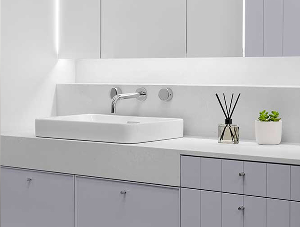 Minimalist bathroom with gray cabinets, white sink, wall-mounted faucet, reed diffuser, and a small plant.
