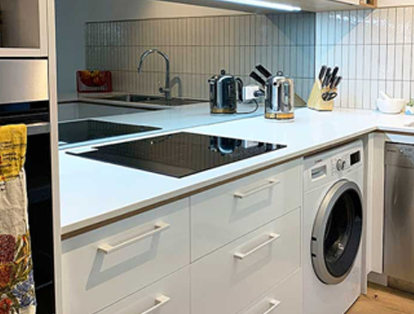 Modern kitchen corner with white cabinets, stovetop, oven, washing machine, knives, and toaster on counter. Modern kitchen corner with white cabinets, stovetop, oven, washing machine, knives, and toaster on counter.