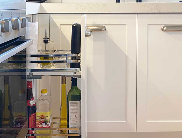 A kitchen cabinet with a pull-out shelf holding oil bottles and a glass container beside a stove. A kitchen cabinet with a pull-out shelf holding oil bottles and a glass container beside a stove.