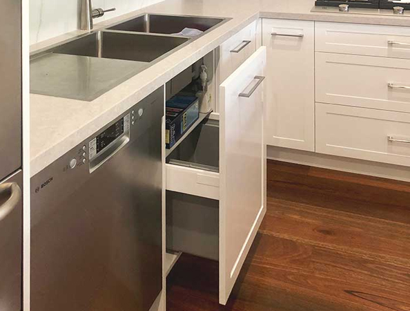 White kitchen with a double sink, a dishwasher, and an open pull-out trash cabinet, on wooden flooring. White kitchen with a double sink, a dishwasher, and an open pull-out trash cabinet, on wooden flooring.