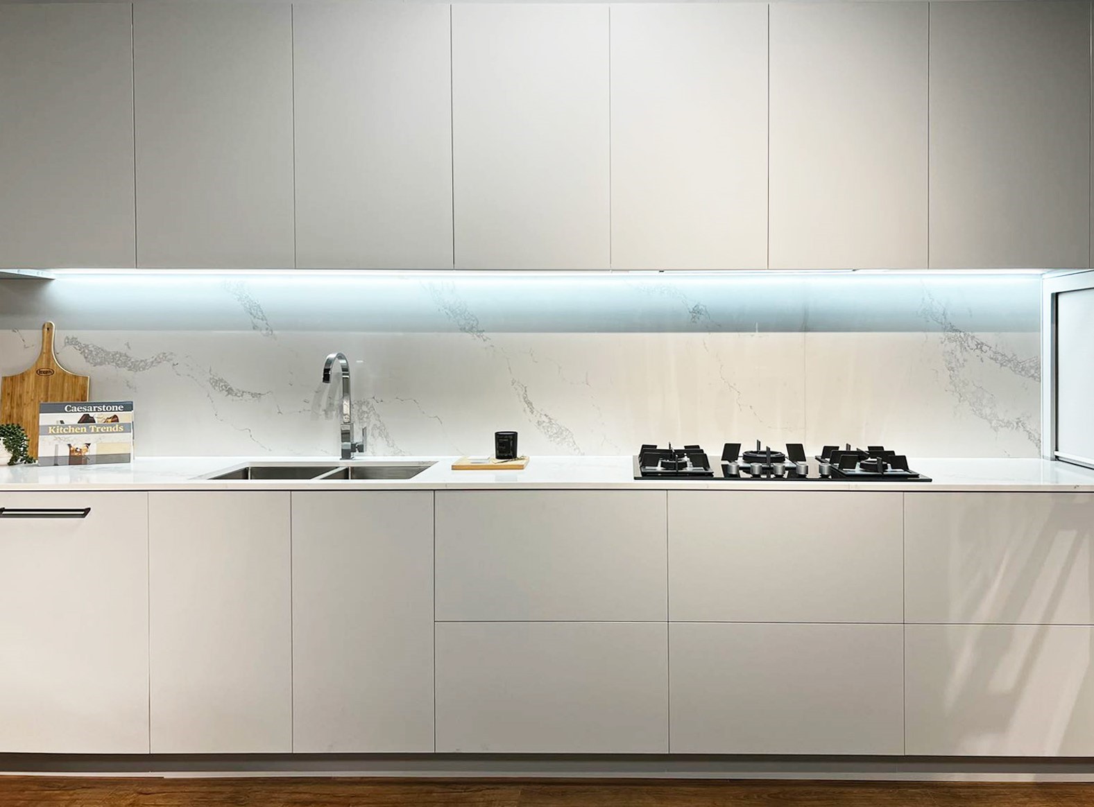 Modern minimalist kitchen with sleek white cabinets, marble backsplash, and gas stovetop on wooden floor.