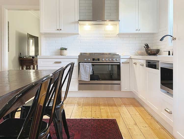 Modern kitchen with white cabinets, stainless steel appliances, and a wooden floor. Red rug and black chairs by the table.