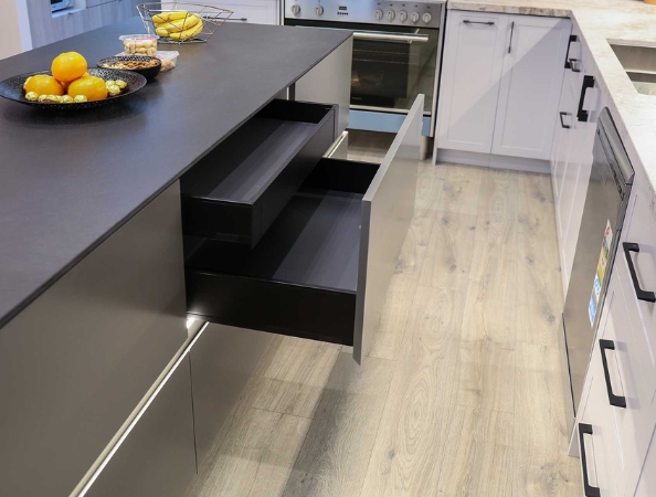Modern kitchen with an open drawer on a black island, fruit bowl, and sleek appliances under soft lighting.