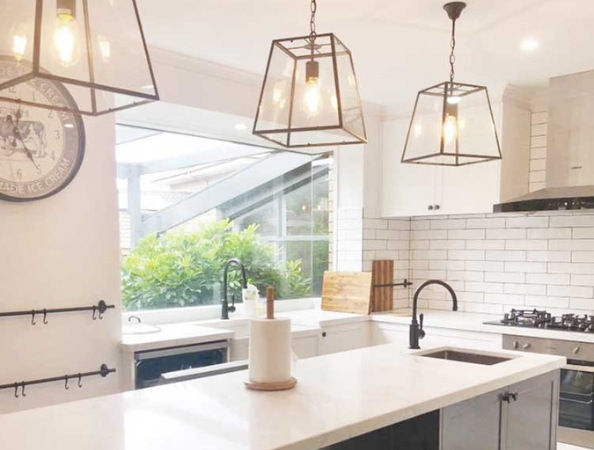 Modern kitchen with white cabinets, subway tiles, large island, pendant lights, and a window with greenery outside.