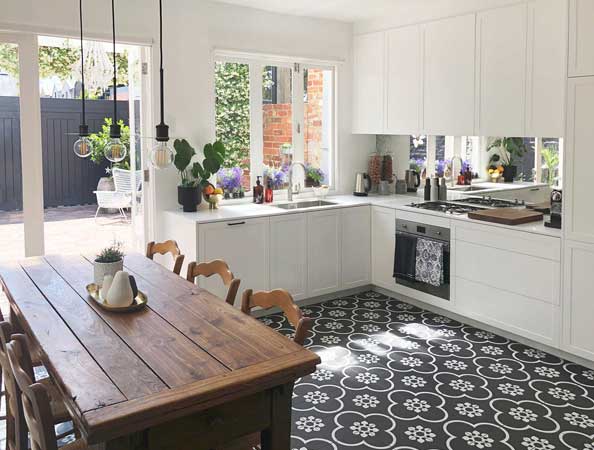 Bright kitchen with white cabinets, patterned tile floor, wooden dining table, and large windows opening to a patio.