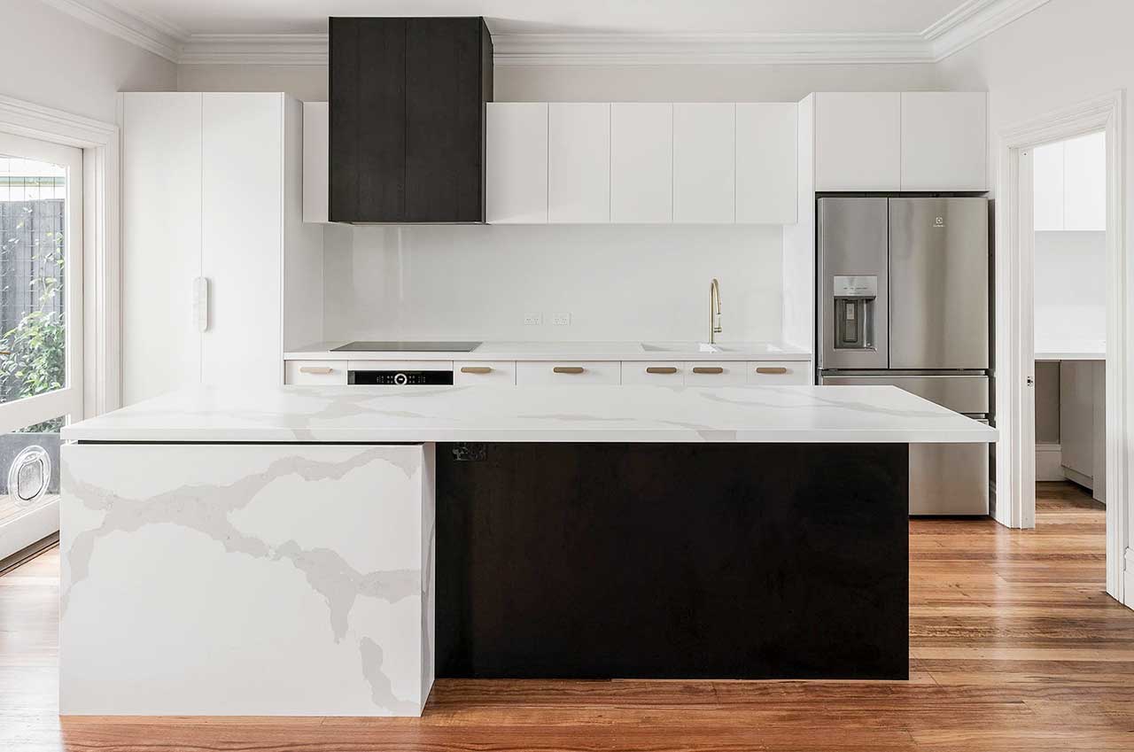 Modern kitchen with white cabinets, black accents, stainless steel fridge, and wooden floor.