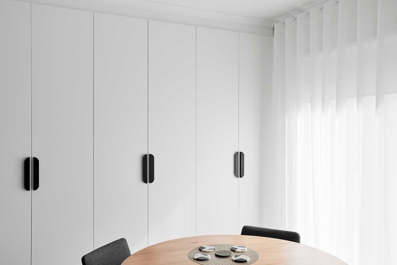 Minimalist room with white cabinets, round wooden table, black chairs, and sheer curtains. Minimalist room with white cabinets, round wooden table, black chairs, and sheer curtains.