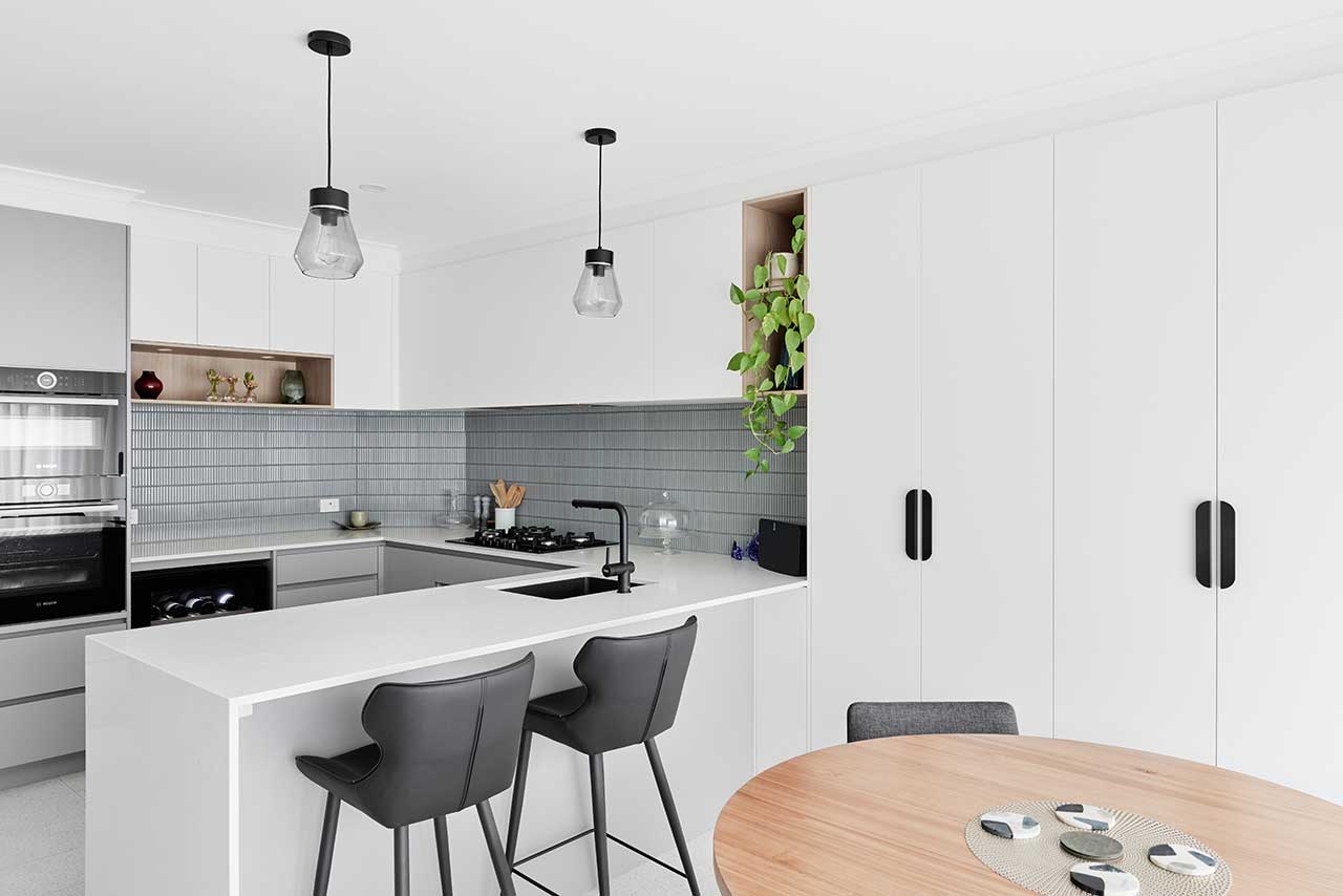 Modern kitchen with white cabinets, grey backsplash, black barstools, pendant lights, and a round wooden table. Modern kitchen with white cabinets, grey backsplash, black barstools, pendant lights, and a round wooden table.