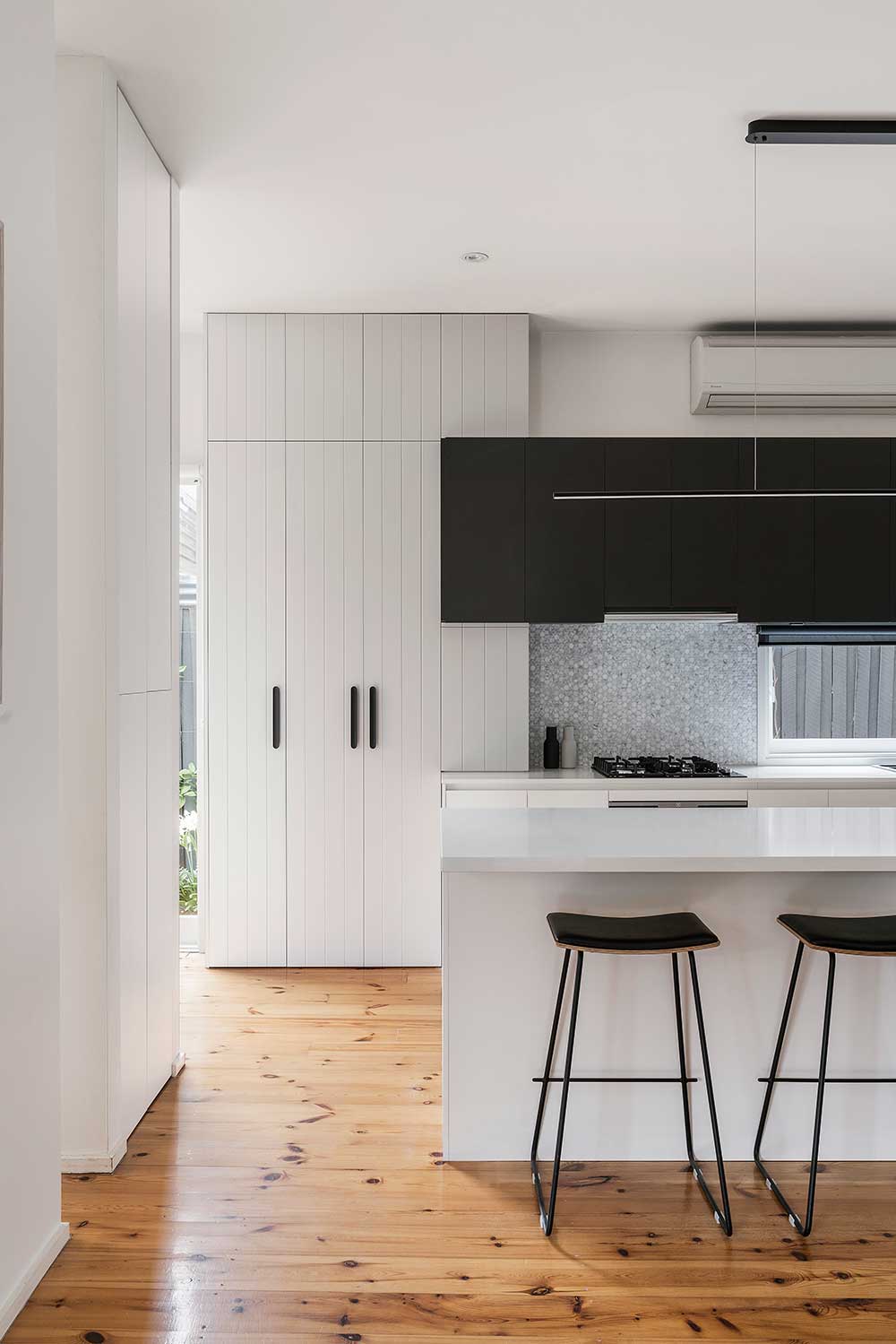 Modern kitchen with white cabinets, black overhead units, an island with two stools, and wooden flooring. Modern kitchen with white cabinets, black overhead units, an island with two stools, and wooden flooring.