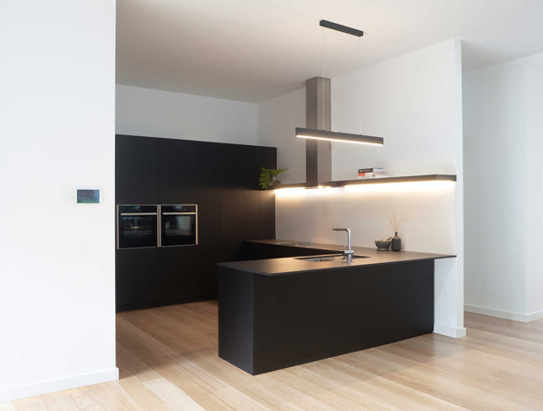 Minimalist kitchen with dark cabinets, island with sink, slim pendant lights, and light wooden flooring.