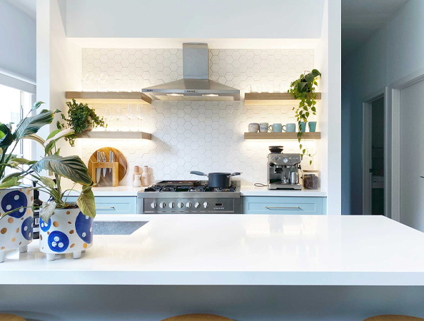 Modern kitchen with white countertops, plants, a stovetop, shelves, and hexagonal backsplash tiles.