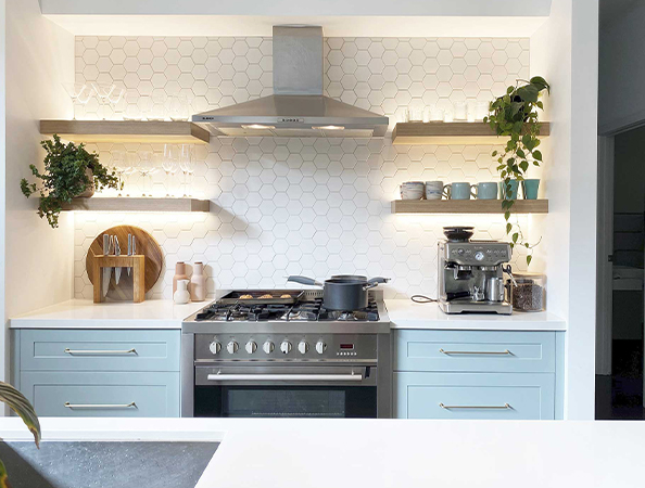 Modern kitchen with light blue cabinets, a stainless steel stove, overhead shelves, plants, and a coffee machine. Modern kitchen with light blue cabinets, a stainless steel stove, overhead shelves, plants, and a coffee machine.