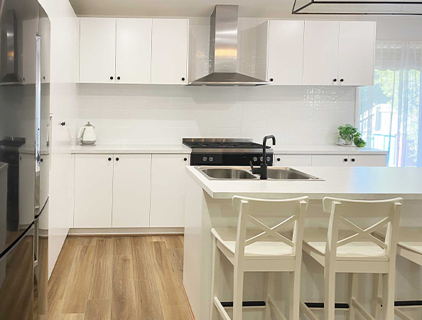 Modern kitchen with white cabinets, a stainless steel range hood, island with sink, and two white barstools. Modern kitchen with white cabinets, a stainless steel range hood, island with sink, and two white barstools.