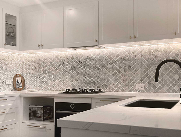 Modern kitchen with white cabinets, marble backsplash, and black faucet. Under-cabinet lighting highlights the design. Modern kitchen with white cabinets, marble backsplash, and black faucet. Under-cabinet lighting highlights the design.