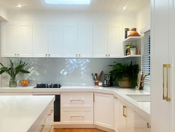 A modern white kitchen with plants, a gas stove, and a blender on the countertop. A modern white kitchen with plants, a gas stove, and a blender on the countertop.
