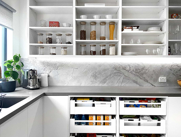 Modern kitchen with open shelves, glass jars, drawers, plant by the sink, and marble backsplash.