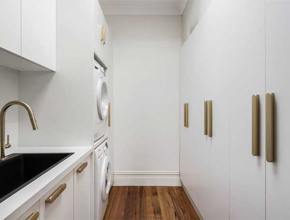 Modern laundry room with white cabinets, stacked washer and dryer, a black sink, and wooden floor.