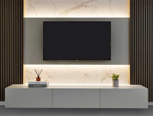 Minimalist entertainment center with mounted TV, white cabinet, plant, and book against a backlit marble wall.