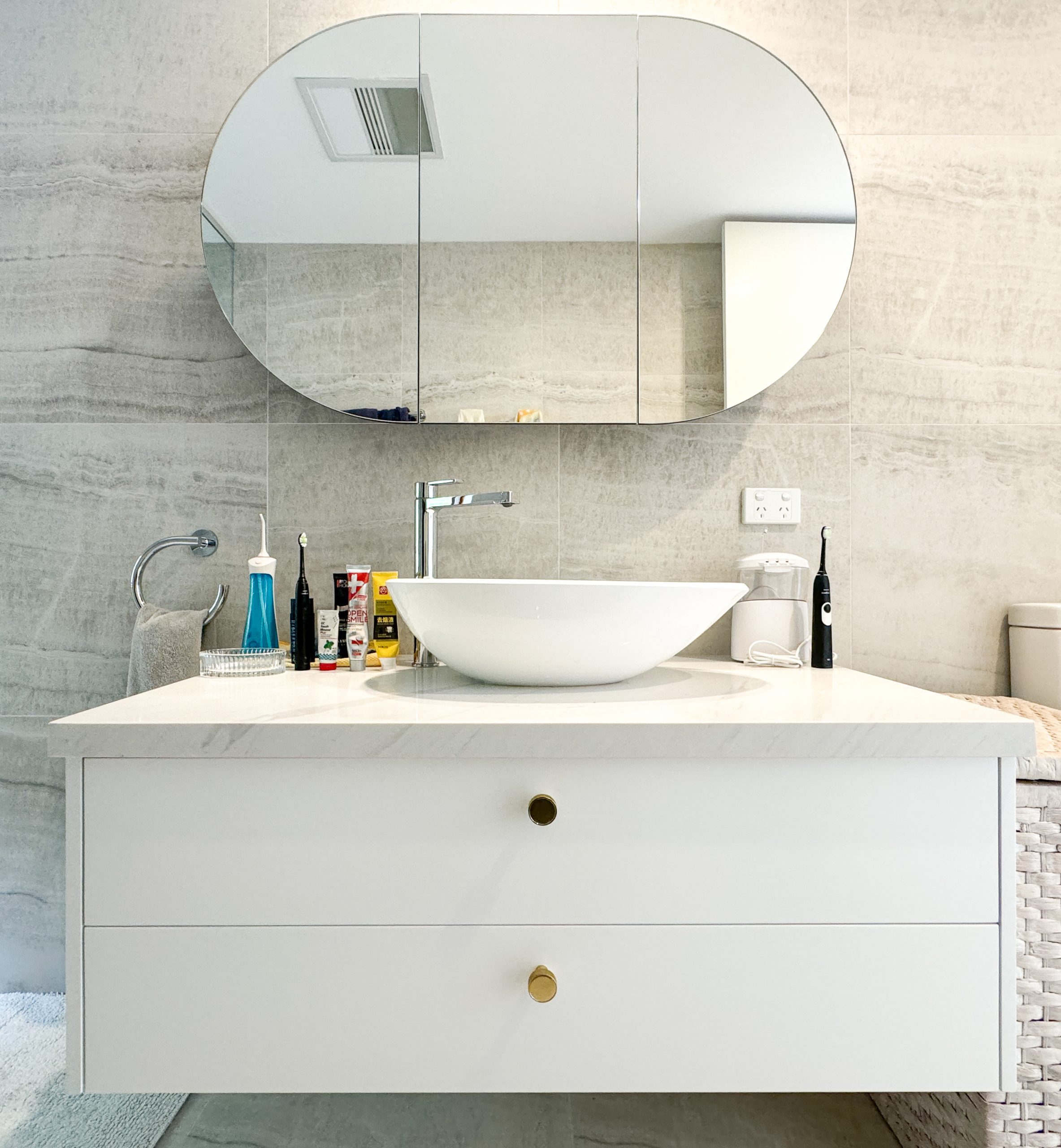 Modern bathroom with an oval mirror, white countertop, round sink, and various toiletries beside it. Modern bathroom with an oval mirror, white countertop, round sink, and various toiletries beside it.