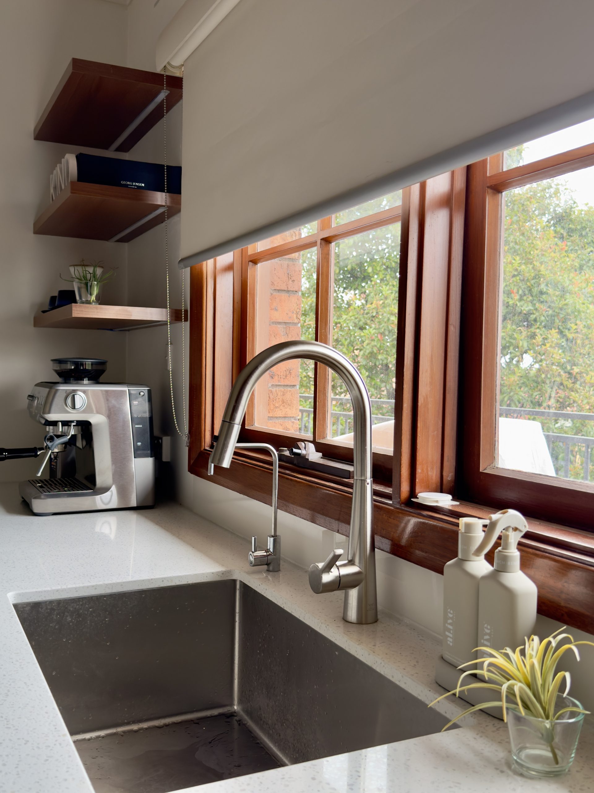 Kitchen sink with a stainless steel faucet, coffee machine, and soap bottles near a window. Kitchen sink with a stainless steel faucet, coffee machine, and soap bottles near a window.