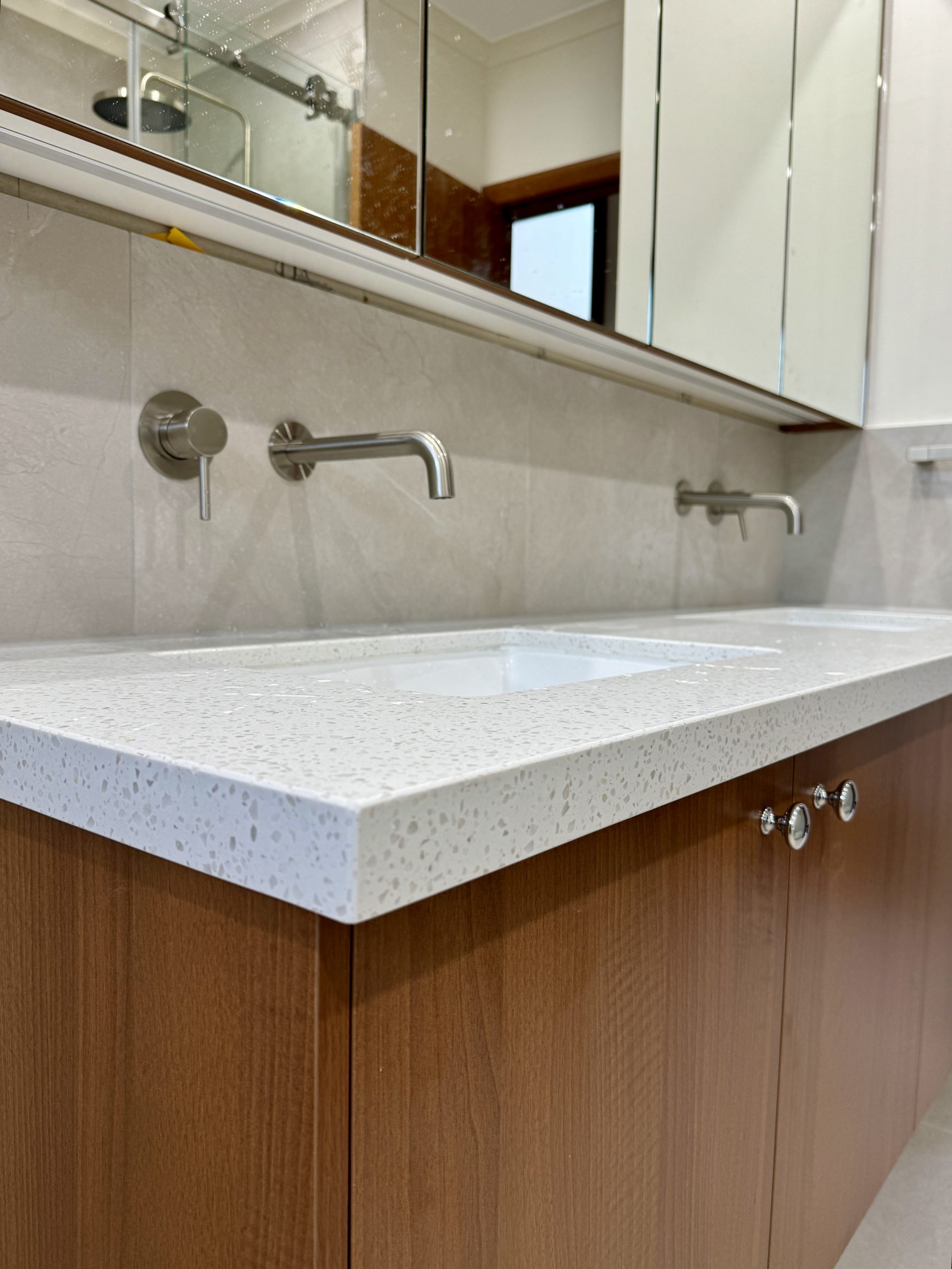Modern bathroom with white countertop, wooden cabinets, twin sinks, and stainless steel faucets. Modern bathroom with white countertop, wooden cabinets, twin sinks, and stainless steel faucets.