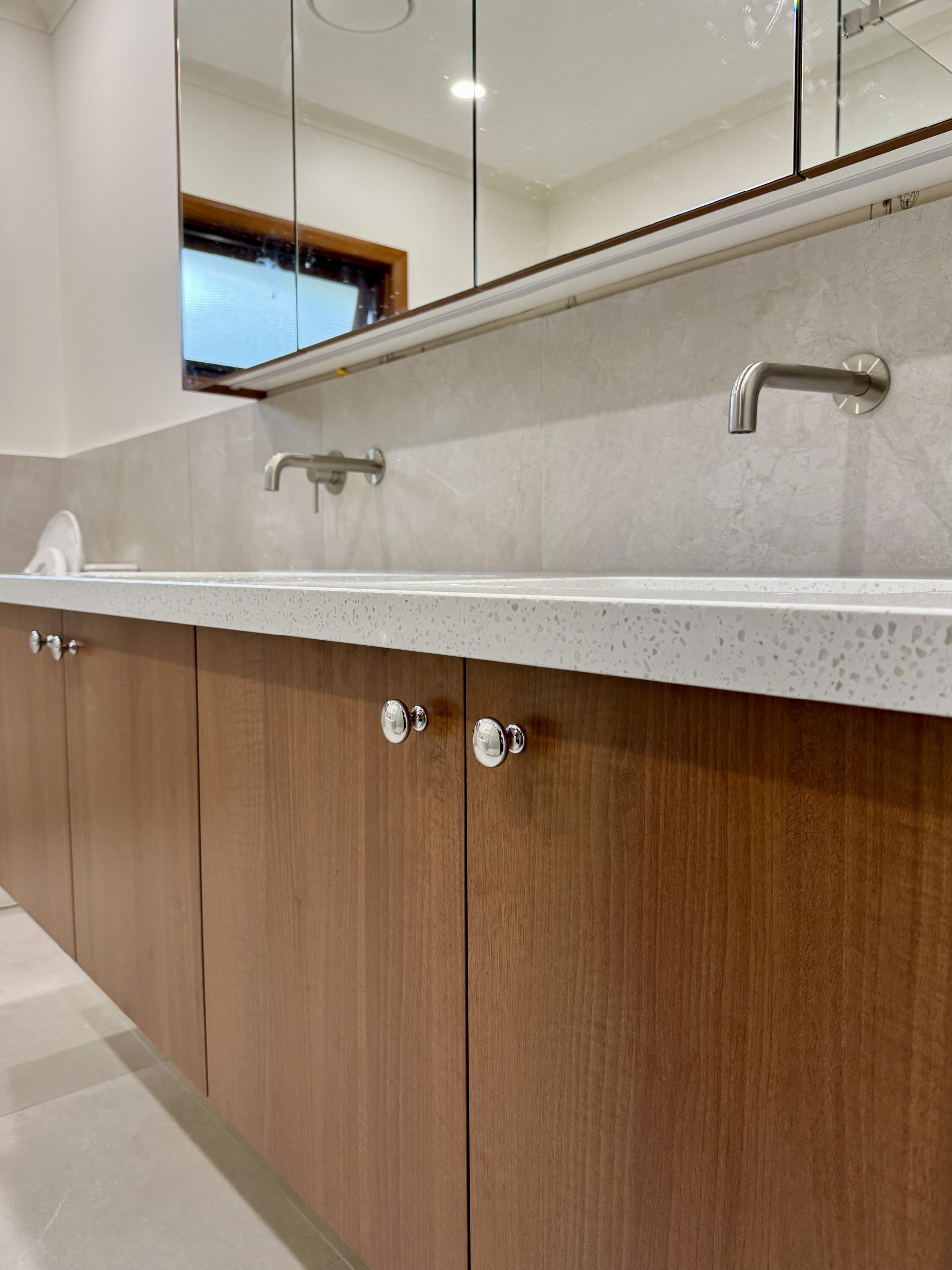 Modern bathroom sink with brown wooden cabinets and a large mirror above. Modern bathroom sink with brown wooden cabinets and a large mirror above.