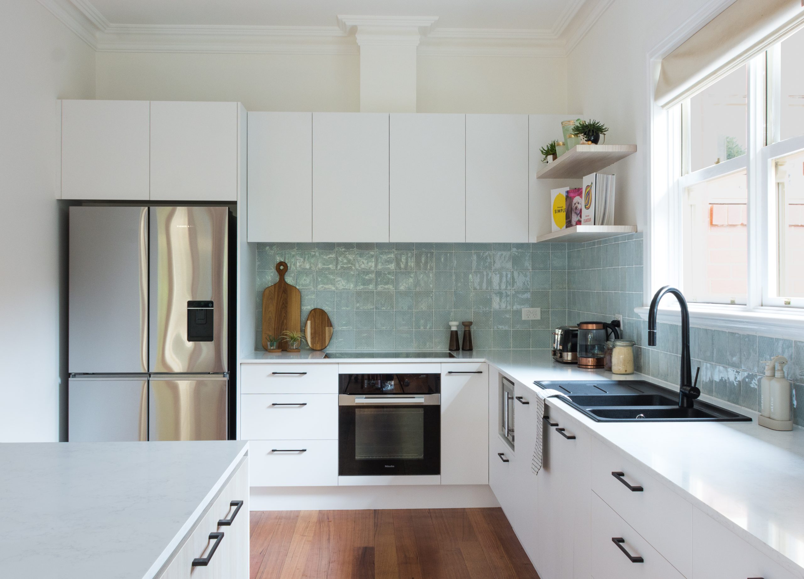 Modern kitchen with white cabinets, stainless steel appliances, and light blue tile backsplash. Natural light from window.