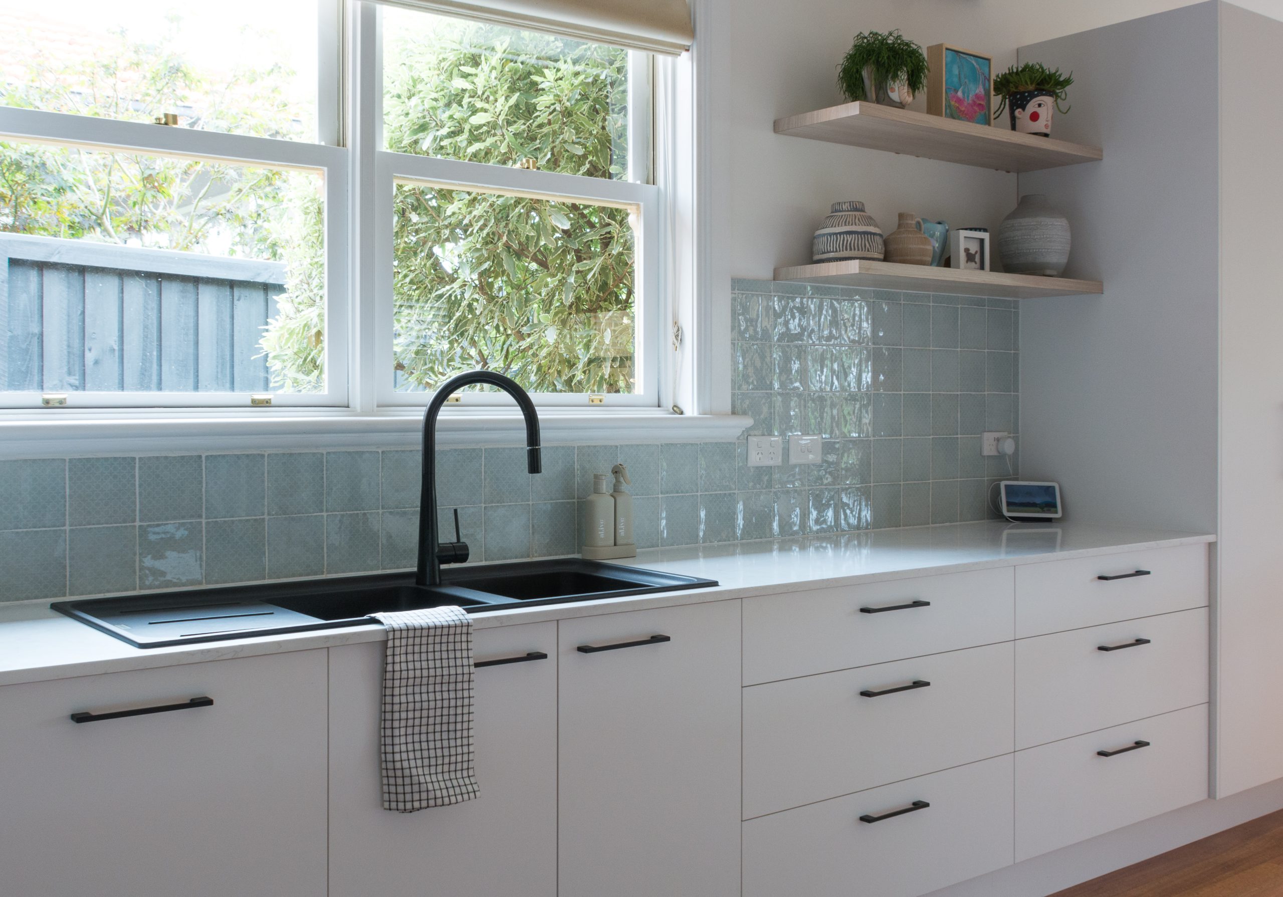 Modern kitchen with white cabinets, black fixtures, tiled backsplash, and decorative shelves near a window. Modern kitchen with white cabinets, black fixtures, tiled backsplash, and decorative shelves near a window.
