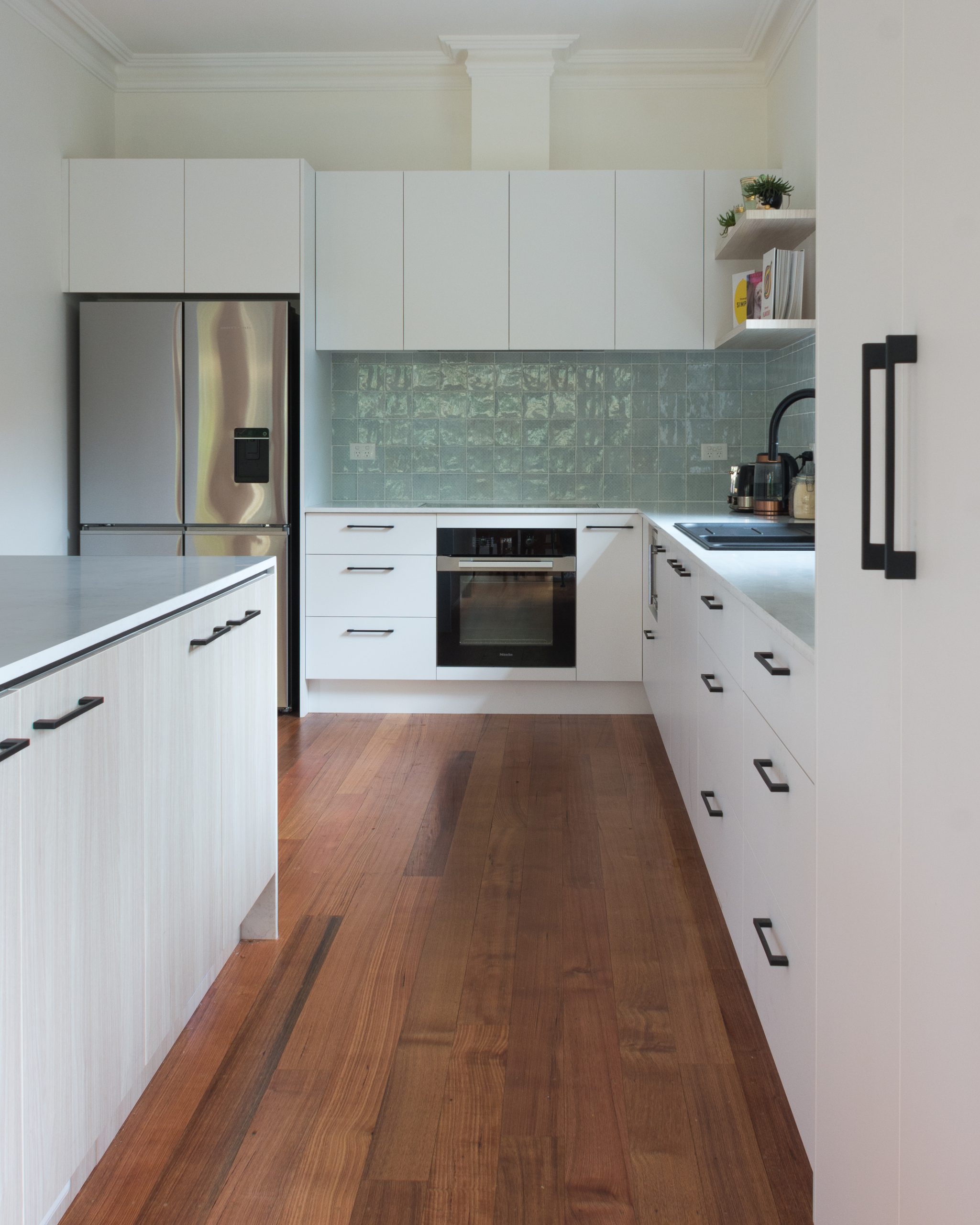 Modern kitchen with wooden floors, white cabinets, stainless steel appliances, and a green tile backsplash. Modern kitchen with wooden floors, white cabinets, stainless steel appliances, and a green tile backsplash.